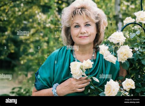 59 Year Old Woman In The Garden A Mature Woman Enjoys The Flowers Of A Rose Grown With Her Own