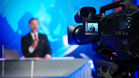 Professional TV Camera Standing in Live News Studio with Anchor seen in Small Display. Unfocused ...