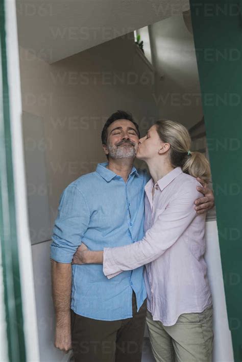 Mature Woman Kissing Husband Standing At Home Stock Photo