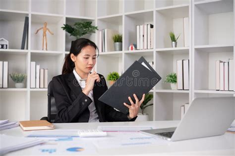 Focused Asian Female Accountant Doing Paperwork In Office With Plan