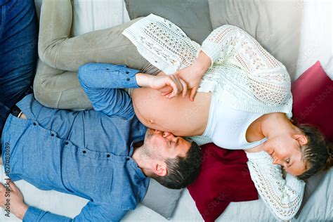 Expectant Parents Sleeping On The Sofa While The Father Gently Kisses The Mother S Naked Baby