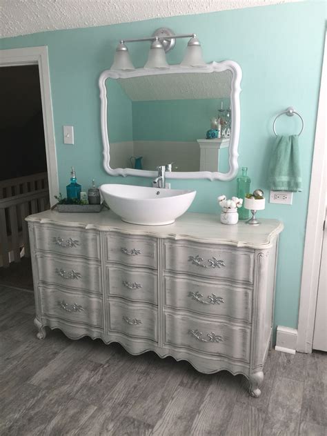 A White Sink Sitting On Top Of A Wooden Dresser Next To A Wall Mounted