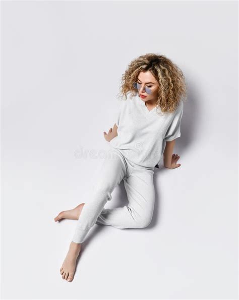 Blonde Krullende Vrouw In Gerookte Glazen Witte Broek En Blouse Zit Op De Vloer Met Haar Blote