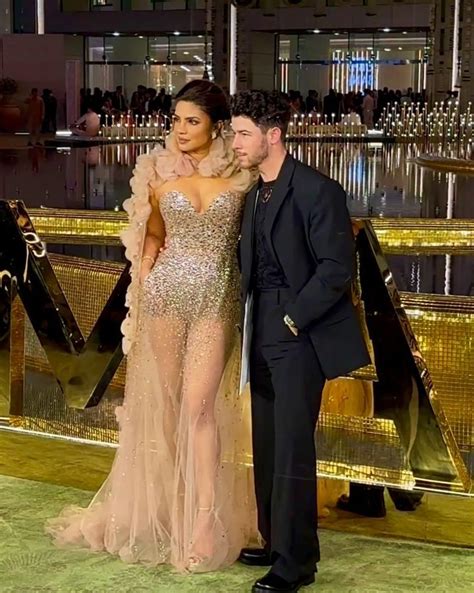 A Man And Woman Standing Next To Each Other In Front Of A Bar With Gold