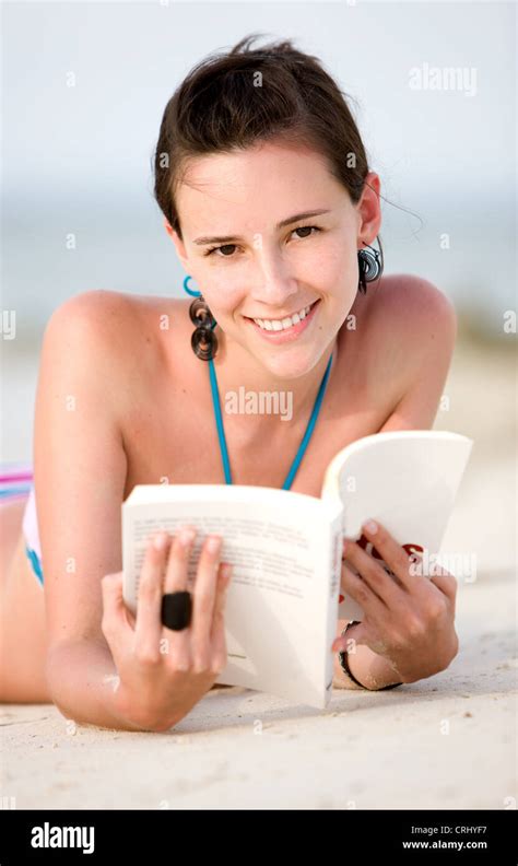 glückliche junge Frau im Bikini am Strand liegend ein Buch lesen