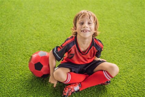 Premium Photo | Little cute kid boy in red football uniform playing ...