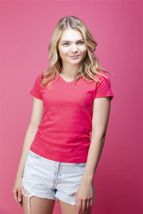 Happy Winsome Caucasian Blond Girl In Coral T Shirt Posing In Summer Shorts While Showing