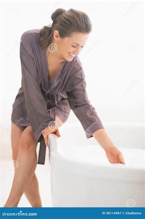 Happy Young Woman Checking Water Temperature In Bathtub Stock Image