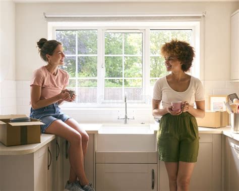 Two Female Friends Or Same Sex Couple Taking A Coffee Break From Unpacking On Moving Day In New