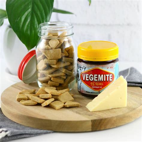 a wooden cutting board topped with cheese and crackers next to a jar of vegemite