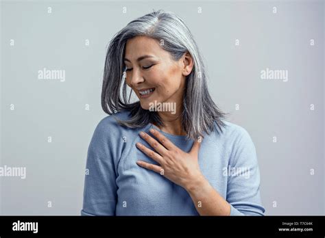 Beautiful Mature Asian Grey Haired Woman Touches Her Chest Gratefully And Smiles Coquettishly In