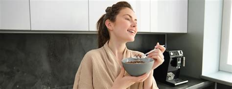 Free Photo Goodlooking Brunette Woman Eating Her Breakfast Standing In Kitchen Near Worktop