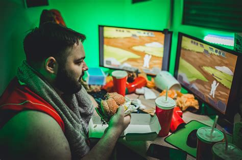 Overweight Gamer Playing Video Games And Eating A Burger Stock Photo