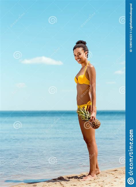 Smiling African American Woman In Bikini Holding Pineapple On Sandy