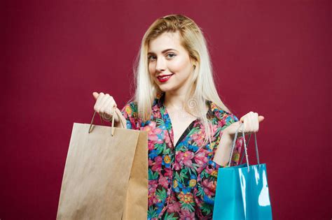 Portrait Of Cute Blonde With Two Paper Bags In Colorful Shirt On Pink