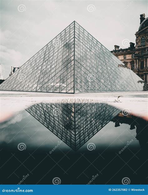 Vertical Shot Of The Famous Louvre Museum Reflected On A Water Puddle