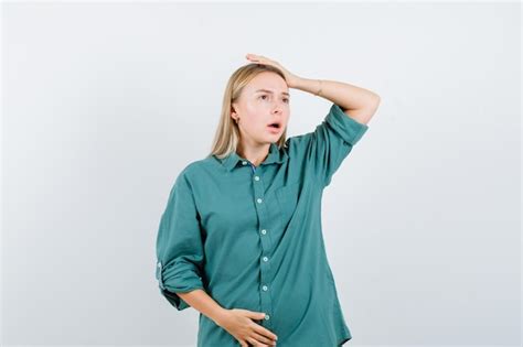 Fille blonde mettant la main au dessus de la tête tout en tenant la main sur le ventre en blouse