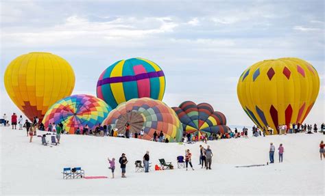 Many Hot Air Balloons Are Being Flown In The Sky On A Beach With People