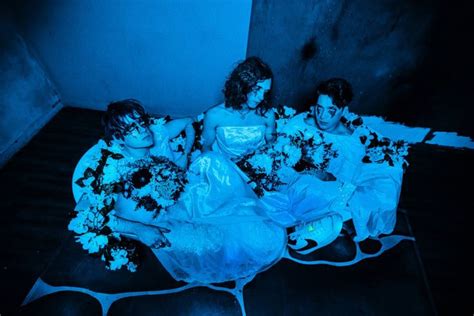 Three Women In White Dresses Sitting On The Floor With Bouquets Of