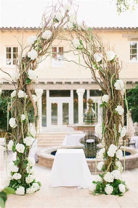 An Archway Decorated With White Flowers And Greenery For A Wedding