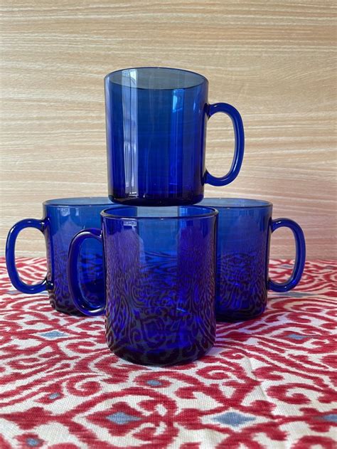 Three Blue Glass Mugs Sitting On Top Of A Red And White Tablecloth