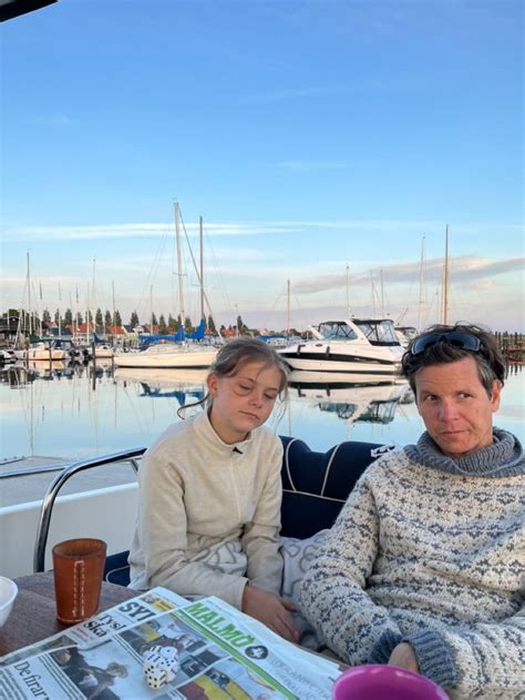 Two People Sitting At A Table On A Boat With Boats In The Water Behind Them