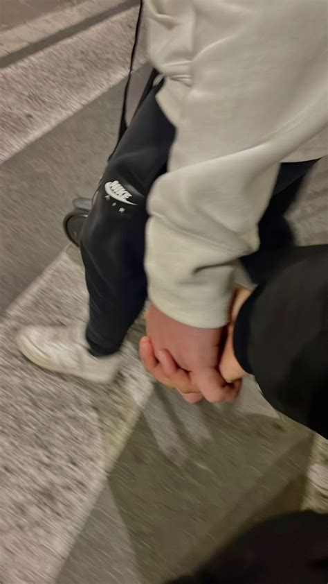 Two People Holding Hands While Walking Down An Airport Walkway With