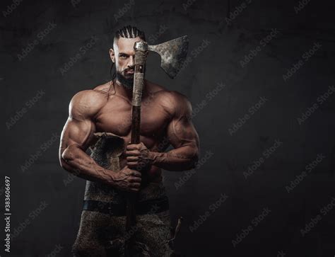 Bodybuilder In Fashion Of Furious Viking Posing Holding Axe Near Face With Naked Torso In Dark
