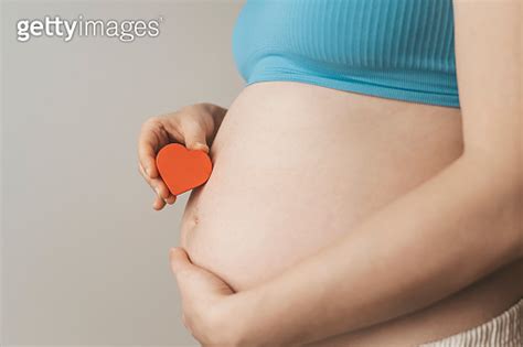 A Pregnant Woman After IVF Holds A Small Red Heart In Her Hands The