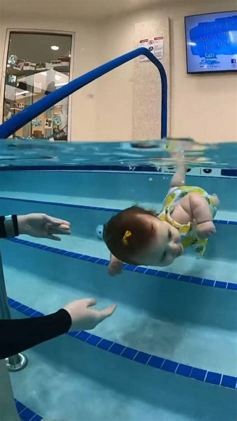 A Baby Swimming In An Indoor Pool While Someone Is Holding Their Hand