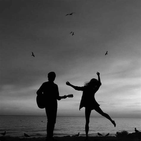 Two People Standing On The Beach With Birds Flying In The Air Above