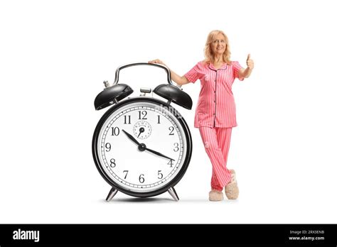 Woman In Pajamas Leaning On A Big Alarm Clock And Gesturing Thumbs Up Isolated On White