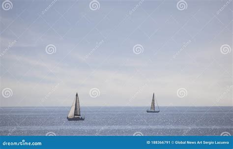 Two Sail Boats Drifting Over The Ocean In Front Of A Wispy Blue Sky