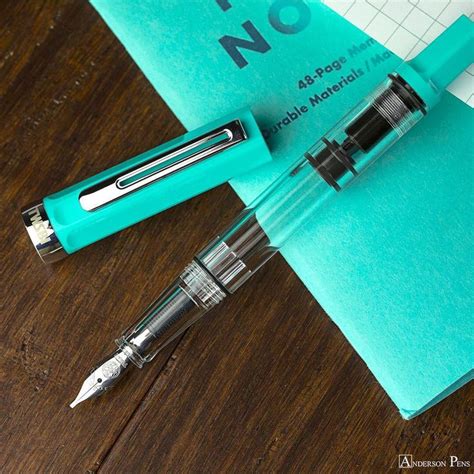 A Fountain Pen Sitting On Top Of A Blue Notebook Next To A Green Notepad