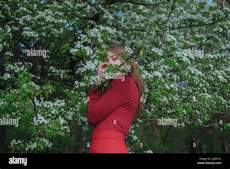 A Blonde Girl In Red Hides In Flowering Trees Stock Photo Alamy