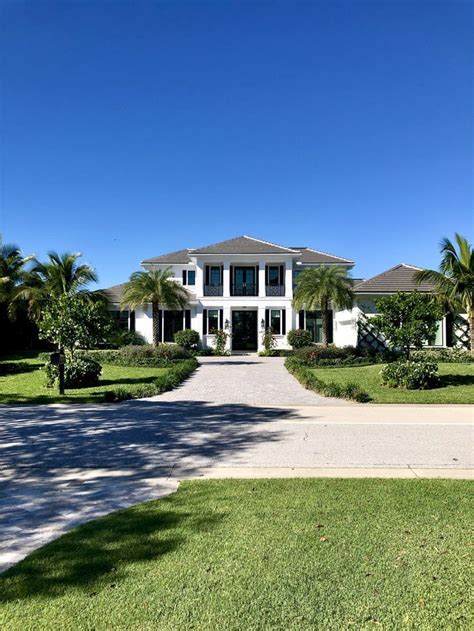 A Large White House Sitting On Top Of A Lush Green Field Next To Palm Trees