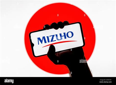 Smartphone with Mizuho Financial Group logo on screen in clenched hand ...