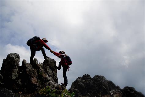 Person Hike Friends Helping Each Other Up A Mountain Man And Woman