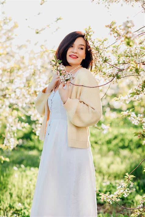 An Attractive Brunette In A White Dress In A Blooming Spring Garden Solar Glare Stock Photo