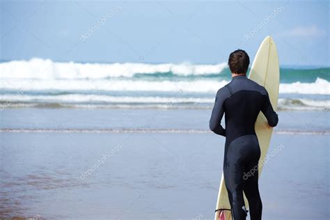 Atractivo joven surfista sosteniendo tabla de surf mientras está de pie