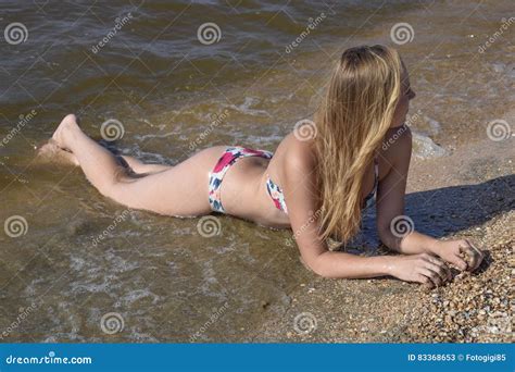 Blond Girl In A Bikini Lying On The Beach And The Waves Splash On It