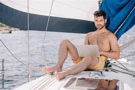 Handsome Shirtless Man In Swim Trunks Using Laptop On Yacht Stock Photo