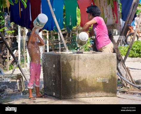 Mother At A Water Tank Whilst Her Daughter Pours Water Over Her Washing Malapascua Island