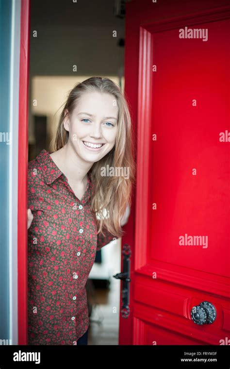 Beautiful Young Woman Opening A Red Door To Welcome Someone Stock Photo