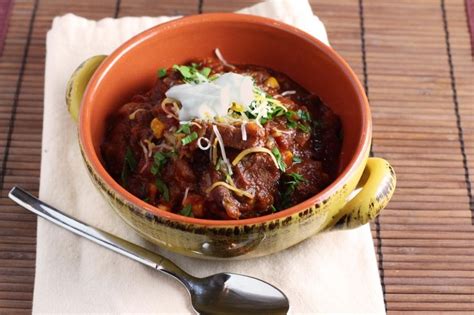 A Bowl Filled With Chili And Sour Cream On Top Of A Napkin Next To A Spoon