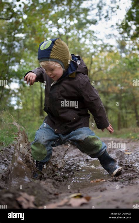 A Little Boy Is Jumping With Joy Into A Muddy Puddle During An Autumn