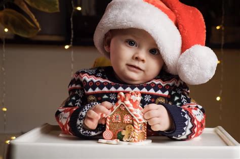 Pequeño y lindo bebé con gorro de papá noel jugando con una casa de pan