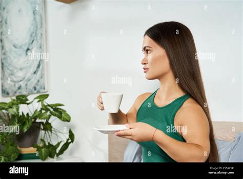 A Petite Brunette Woman Relaxes In Her Cozy Home Savoring Tea While Surrounded By Plants And