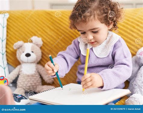 Adorable Hispanic Girl Drawing On Notebook Sitting On Sofa At Home