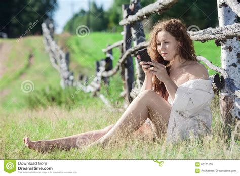 Resting Nude Woman Messaging With A Cellphone While Sitting In Grass In Village Stock Image